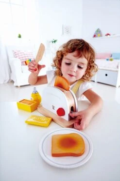 Hape Toaster 7-teilig | Spielküchen-Zubehör -Holzspielzeug-Peitz E3148 Pop up Toaster Set with child 1